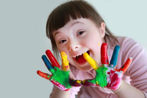 Image of a student with a disability with different colors of paint on her fingers. She is facing the camera and smiling. 