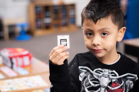 Image of a student holding up a card. The student is in elementary school and is wearing a black shirt. He is in a classroom.